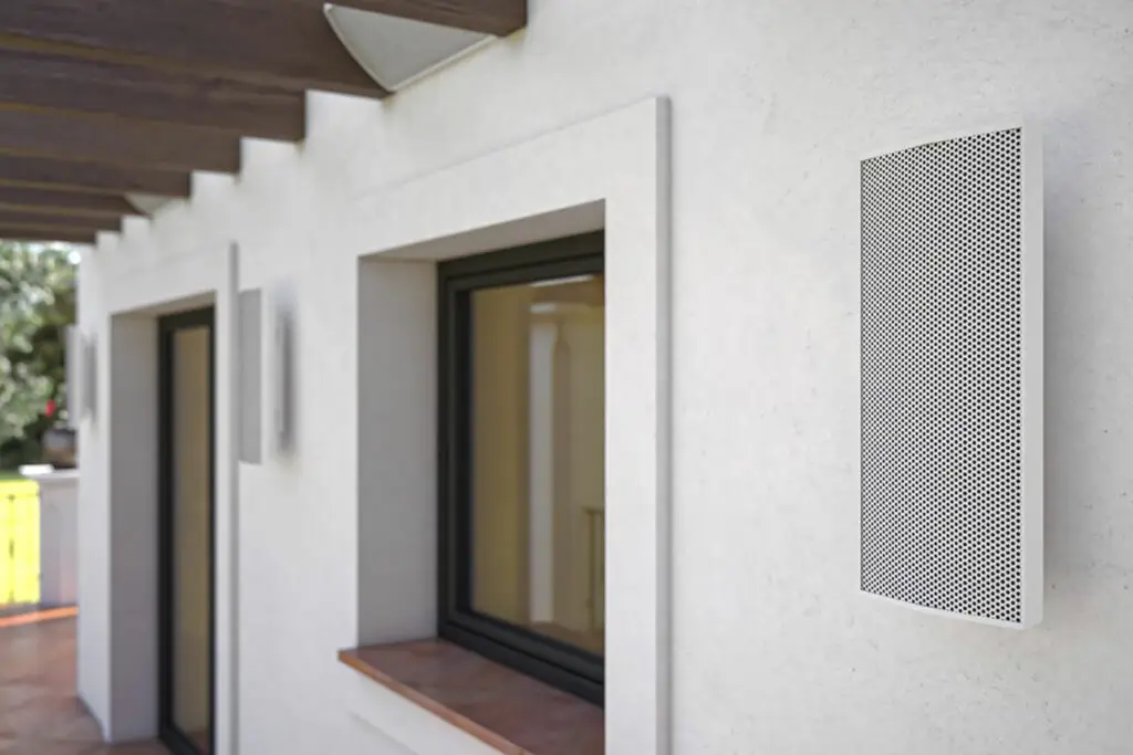 Conscape Lighting + Audio A rectangular outdoor speaker from Conscape Lighting + Audio is mounted on a white exterior wall next to windows and a covered walkway, blending seamlessly with the Toronto lighting ambiance.
